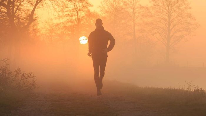 A man jogging through a misty countryside at sunrise, with the sun glowing in the background
