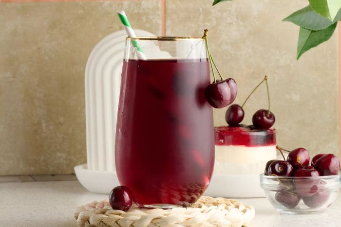 A clear glass of cherry juice alongside fresh cherries on a pristine white table