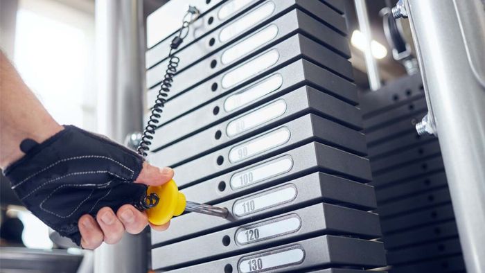 a hand inserting a pin into the weight stack of a gym machine