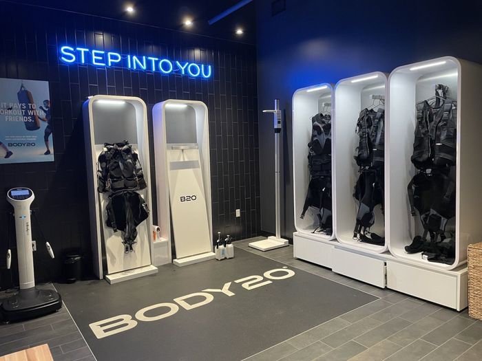 The Body20 suits are neatly arranged in cubbies, displayed beneath a neon sign that reads 'step into you'.