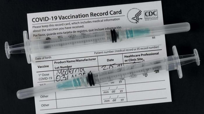 Vaccine card alongside syringes