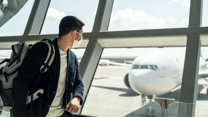 A masked man gazes out of an airport window
