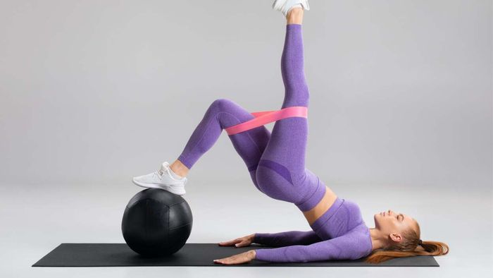 A woman in purple performing an intricate workout routine using a booty band.