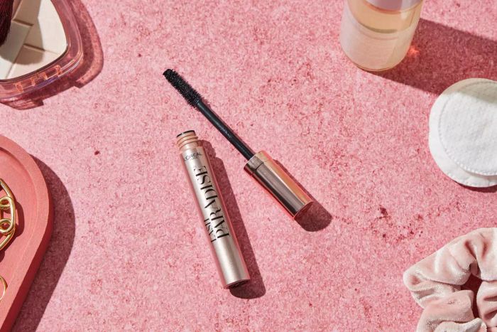 An open tube of L'Oreal Lash Paradise Washable Mascara set against a pink background