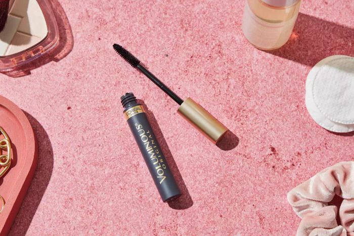 An open tube of L’Oréal Paris Voluminous Original Mascara placed on a pink surface