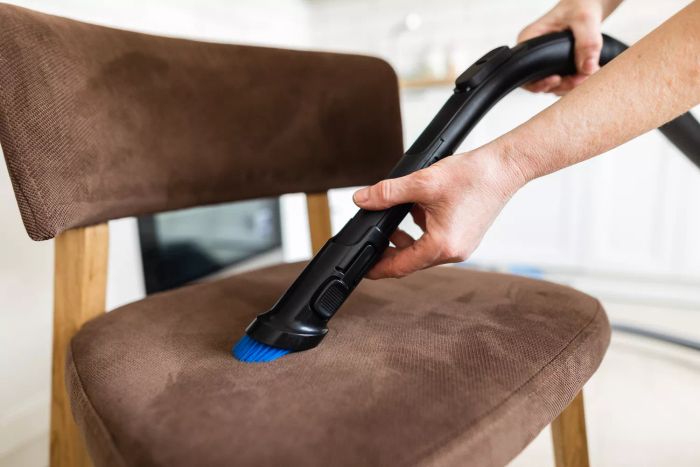 Vacuuming upholstery on a chair using a vacuum attachment in a living room setting.