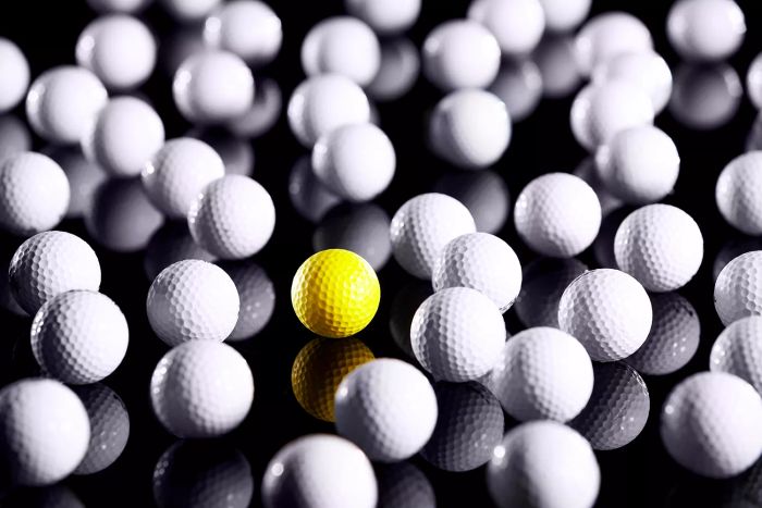 A set of white golf balls, with one distinct yellow ball mixed in.