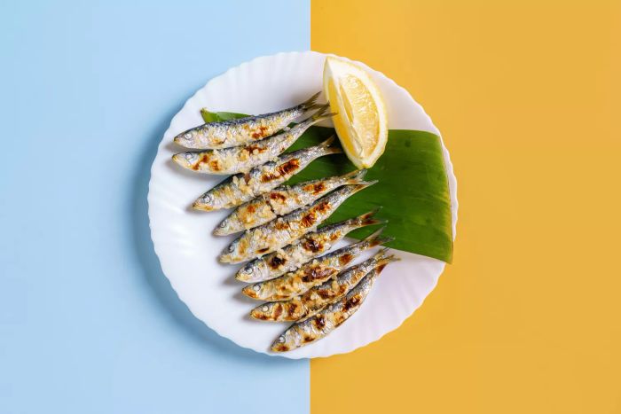 Overhead shot of a plate featuring grilled sardines espetos, set against a vibrant blue and yellow backdrop