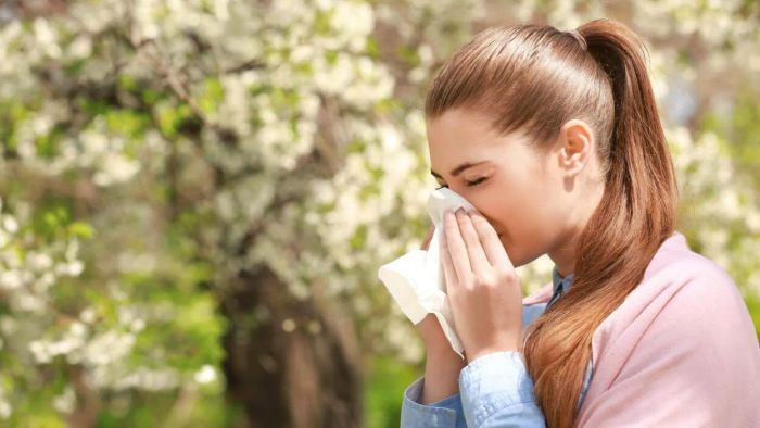 a woman sneezing near blooming trees