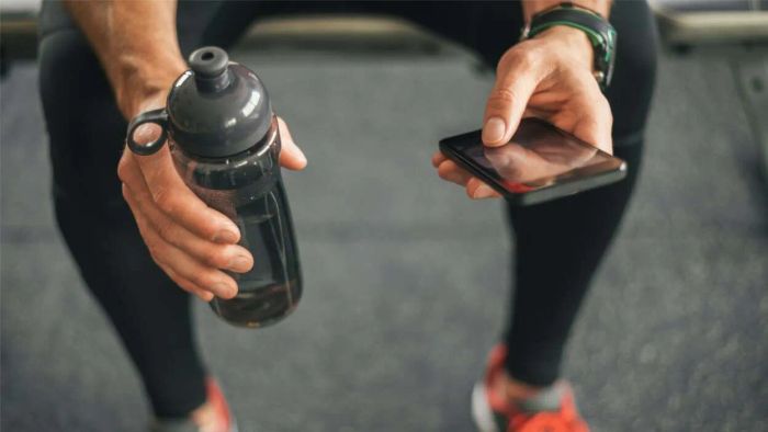 A person holding a water bottle and a phone at the gym