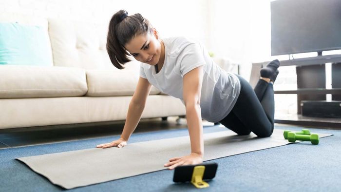 A person performing exercises at home on a yoga mat using light dumbbells