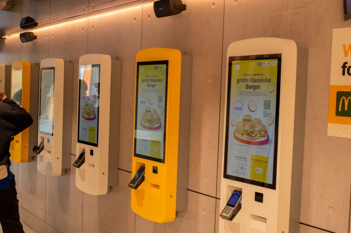 Self-service kiosks inside a fast-food restaurant, showcasing a burger promotion