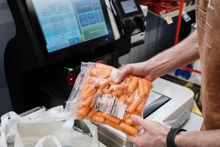 A person scanning a bag of baby carrots at a self-checkout kiosk in a grocery store
