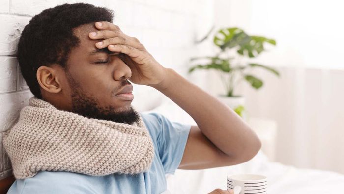a man holding a tea mug, seemingly suffering from a headache