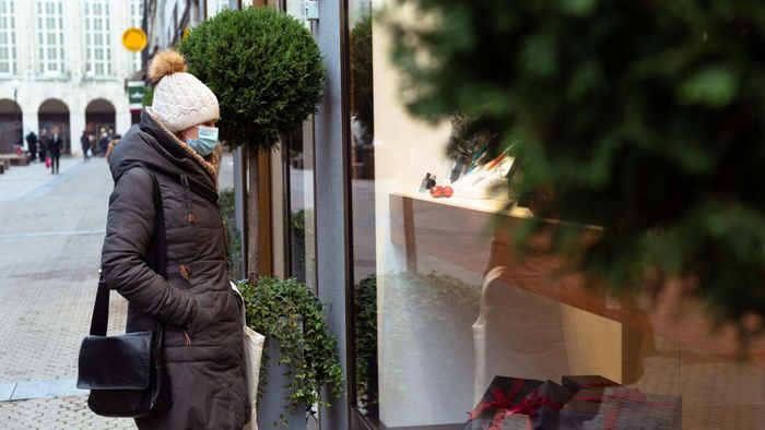 A woman wearing a mask gazes into a storefront window