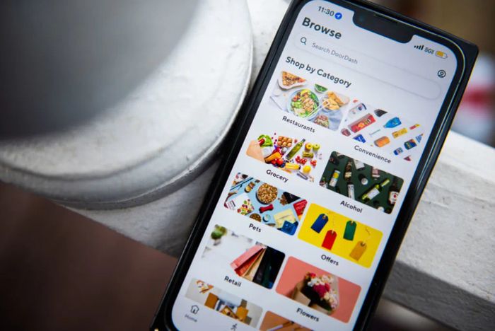 A smartphone showing a food delivery app with sections like restaurants, convenience, and groceries, set against an outdoor background