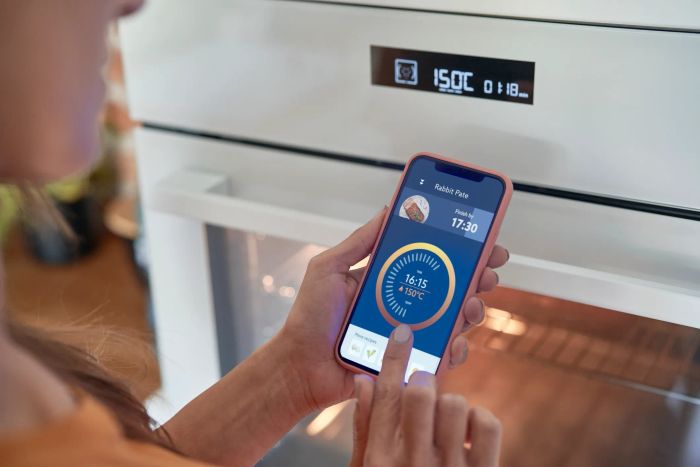 A person using a smartphone app to adjust an oven's temperature and cooking duration, displaying a pie recipe