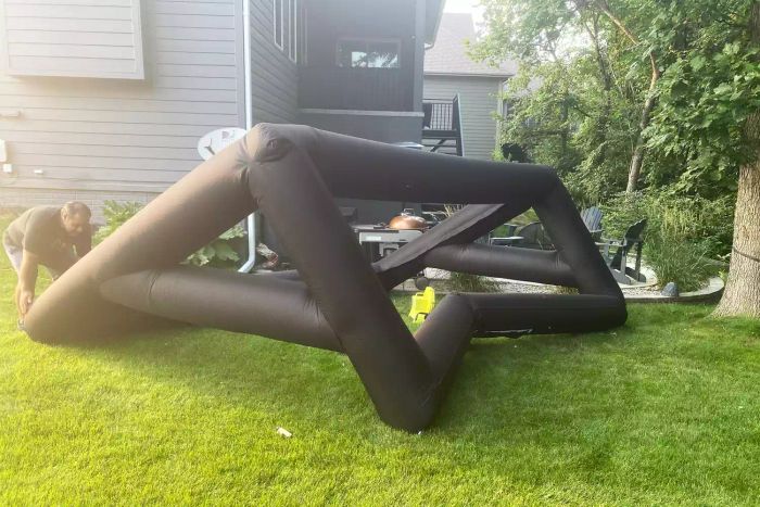 A person setting up the Holiday Styling 19-Foot Giant Inflatable Outdoor Projector Screen in a backyard