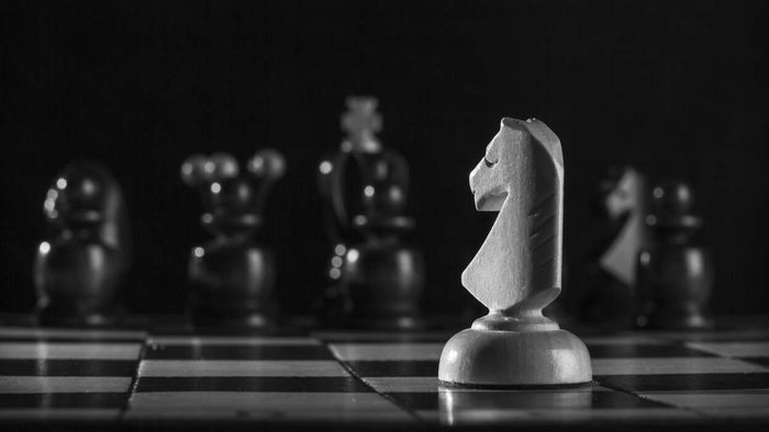 A white knight chess piece confronts a lineup of black pieces