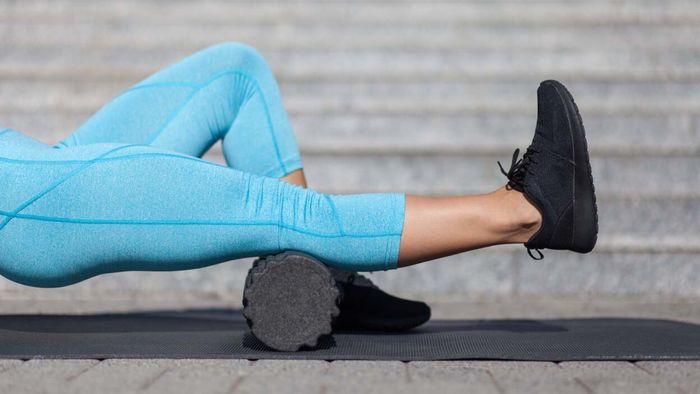 Individual using a foam roller to relieve tension in their calf muscles while wearing blue leggings