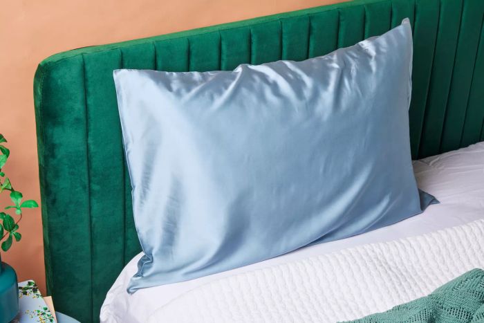 A pillow featuring the Ravmix Mulberry Silk Pillowcase resting against a green velvet headboard.