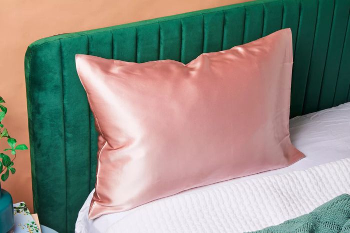The Fishers Finery Mulberry Silk Pillowcase displayed on a pillow against a green velvet headboard.