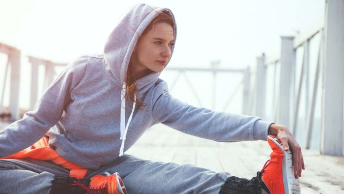 A person in a hoodie performing stretches outside