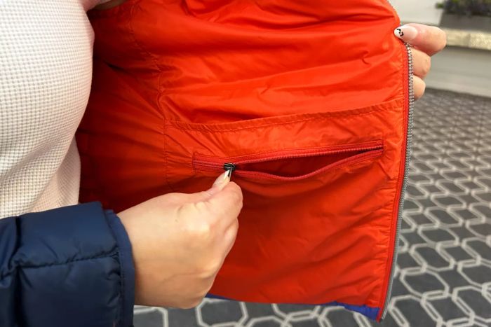 A model demonstrates the inside pocket of the Cotopaxi Women's Fuego Hooded Down Jacket
