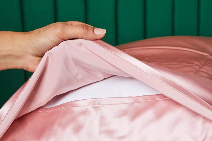 A hand lifting the center fold of the Fishers Finery Mulberry Silk Pillowcase to reveal the pillow inside.