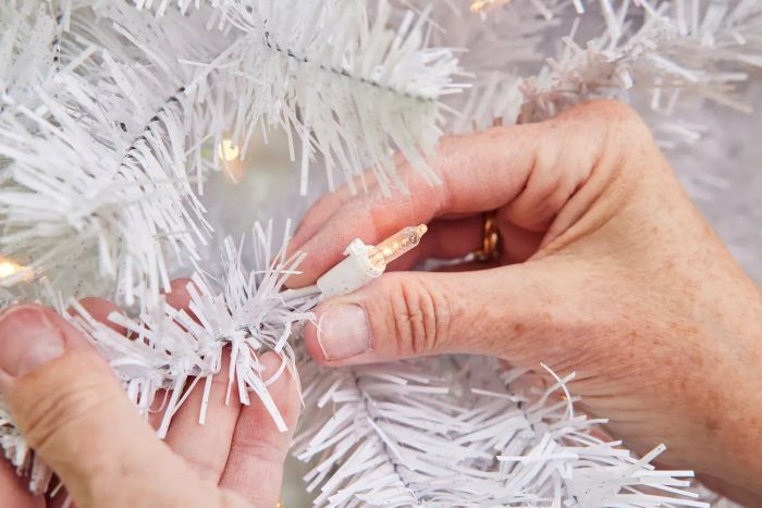 An individual holding a bulb on the National Tree Co Pre Lit White Artificial Christmas Tree
