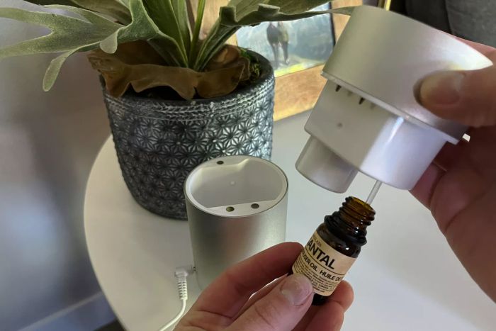 A person holding components of the Eco Nebulizing Diffuser and an essential oil bottle