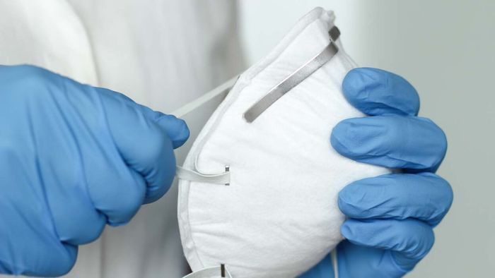 blue-gloved hands holding what looks like an N95 respirator