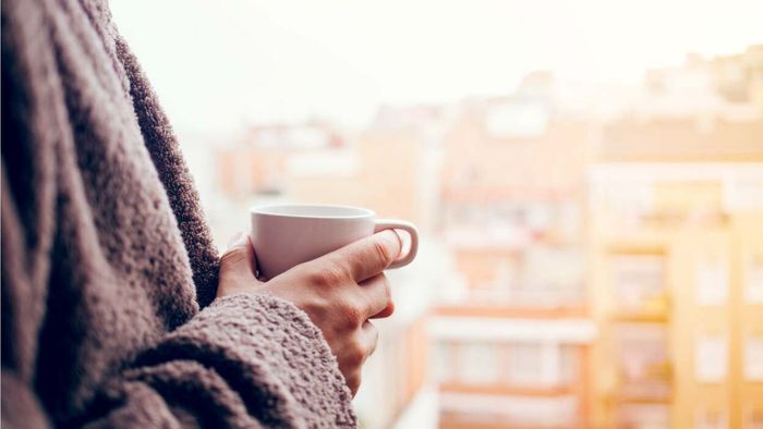 A man stands on a balcony, holding a cup of coffee