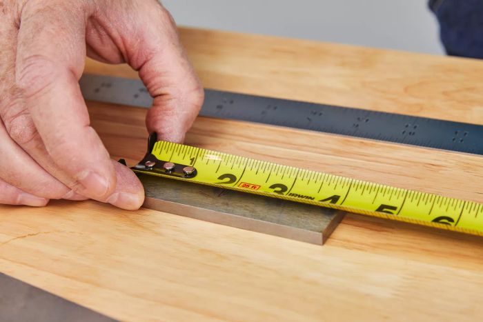 A hand measures a piece of metal on a table using an Irwin Strait-Line Tape Measure