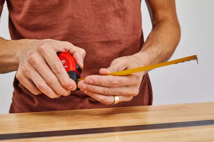 A person extending the Milwaukee Compact Tape Measure over a table alongside a metal ruler
