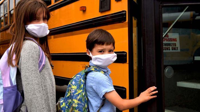 Children in masks prepare to board a school bus