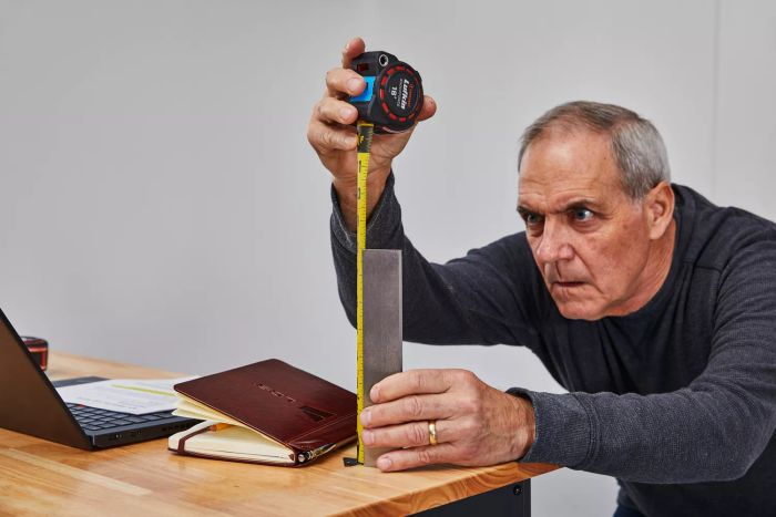 A person measuring a steel piece on a wooden table using the Crescent Lufkin Shockforce Dual-Sided Tape Measure