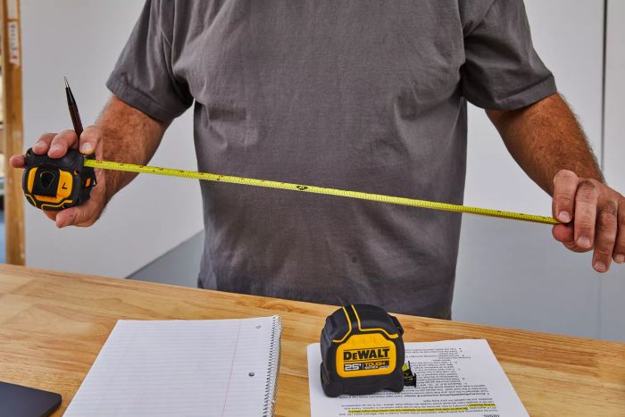 A person extending the DeWalt Tough Series Tape Measure over a wooden table