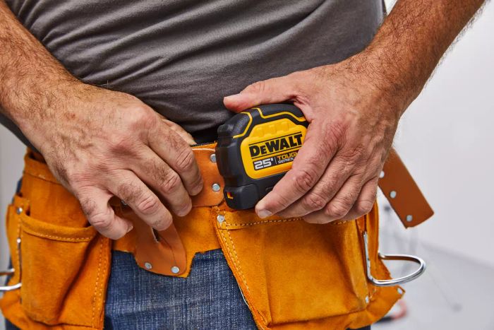 A hand retrieving the DeWalt Tough Series Tape Measure from a hip belt