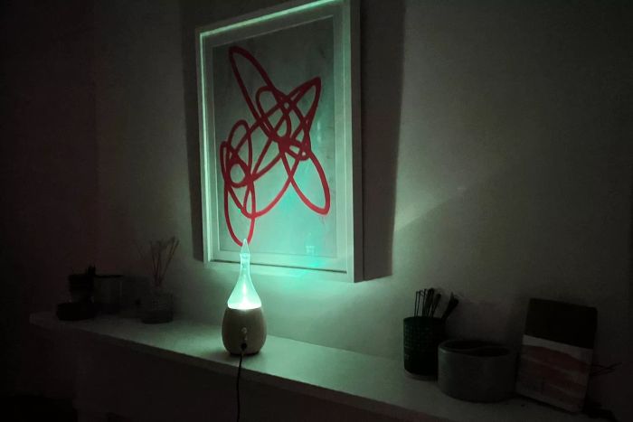 The Organic Aromas Raindrop Nebulizing Diffuser in action on a side table, illuminated by its ambient lights