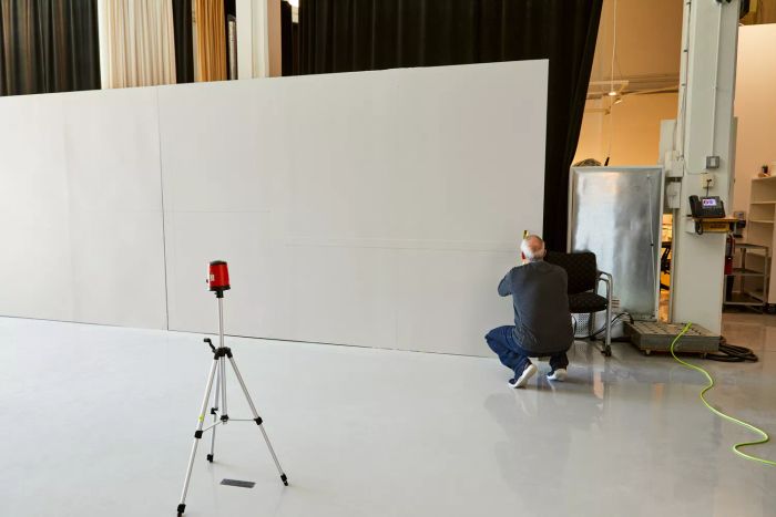 A person measuring a wall using the Johnson Level & Tool 40-0921 Self-Leveling Cross-Line Laser Level Kit