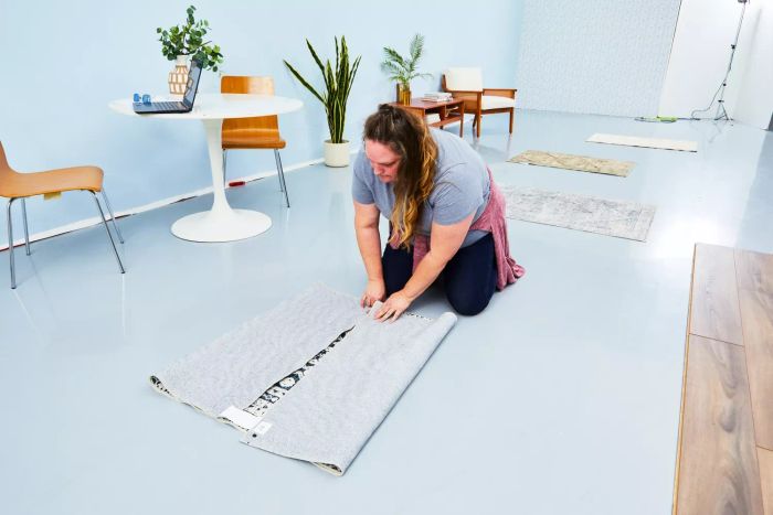 A person folding the World Market Iman Black And Ivory Persian Style Washable Area Rug