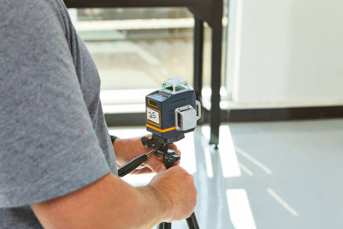 Person adjusting the Cigman 3x360 Degrees Green Laser Level placed on a stand on the floor.