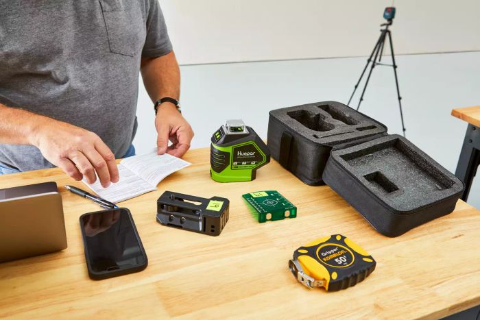 An individual examines the manual for the Huepar 621CG 3D Cross-Line Self-Leveling Green Laser Level on a wooden surface