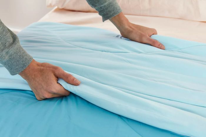 Hands holding the Rest Evercool Cooling Comforter on a bed