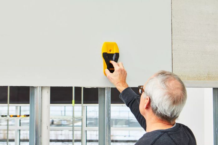 A person locating studs behind a wall using the Dewalt 1-1/2 in. Stud Finder