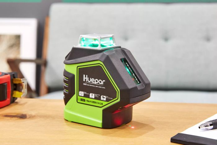 Huepar 3D Laser Level Cross Line shown on a wooden surface alongside a pen and notepad, with the laser illuminated