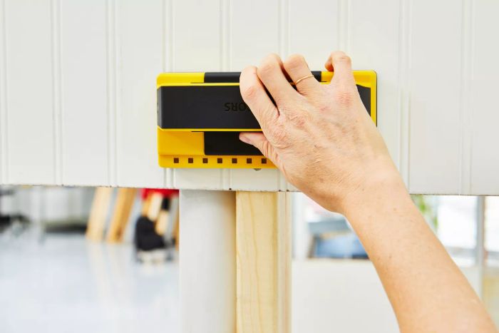 A hand using the Franklin Sensors ProSensor 710 Professional Stud Finder against a wall