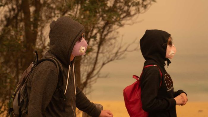 Individuals wearing masks under a haunting orange sky.