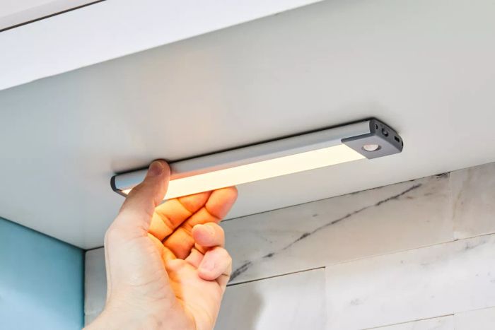 a person installing the Lepotec LED Motion Sensor Cabinet Light in a kitchen